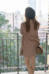 A Hong Kong woman in her 20s with brown hair, wearing a checkered black outfit, a beret, and a mini skirt, gazing at the sea in a scenic park in West Kowloon, Tsim Sha Tsui, Hong Kong.