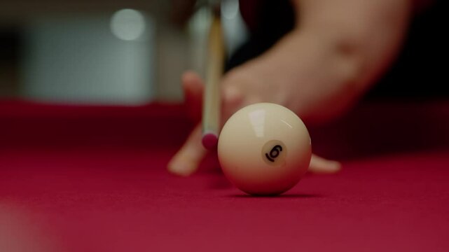 Close-up of a pool cue striking a white ball with the number six on a red pool table. Close up. Slow motion