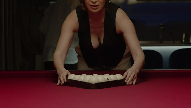 Woman bends over a pool table to arrange the balls in the correct starting position for a game of billiards. Medium shot. Slow motion