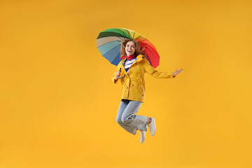 Woman with colorful umbrella jumping on yellow background © New Africa