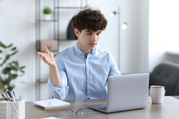 Teenager having video chat via laptop at table indoors. Remote work