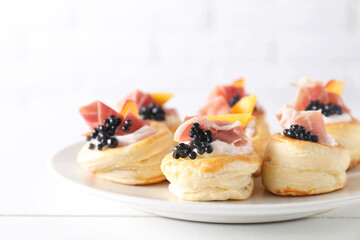 Delicious puff pastry with cream cheese, ham, black caviar and peach on white wooden table