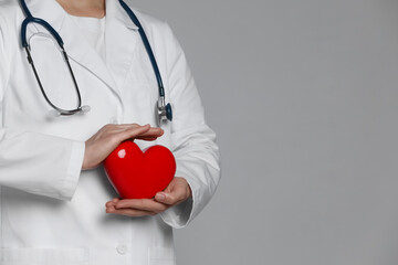 Doctor with red heart on grey background, closeup. Space for text