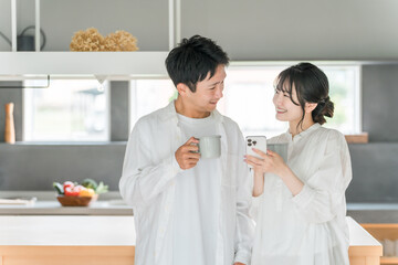 家のダイニングでコーヒーを飲みながらスマホを見る夫婦・カップル
