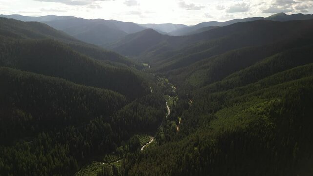 Aerial above Saint Joe Mountains in Idaho with creek and dirt road at sunset