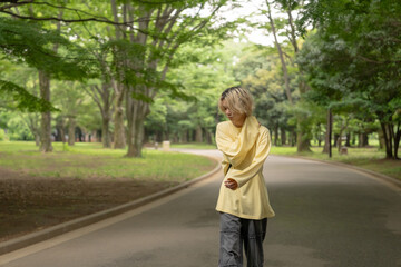 In early summer, a Japanese man in his twenties wearing yellow clothes, walking and strolling through Yoyogi Park, Shibuya, Tokyo, during the day.