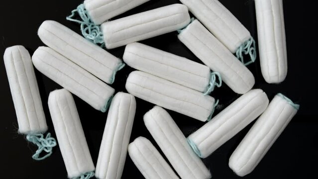 Many tampons rotating, overhead view of standard white tampons on dark background.