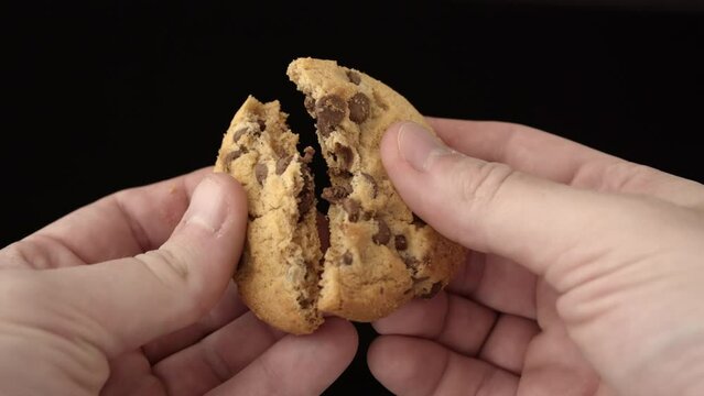 Breaking a chocolate chip cookie in half. male hands hold a cookie and break it in half.