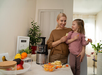 Mother and her cute little daughter making healthy juice from raw vegetables and fruits. Cold press...