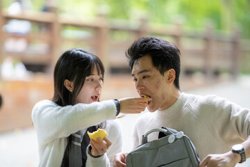 In March, a Taiwanese woman in her twenties and a Hong Kong man are sitting at a table in a lush botanical garden in Zhongzheng District, Taipei City, Taiwan, enjoying bread together and taking walk.