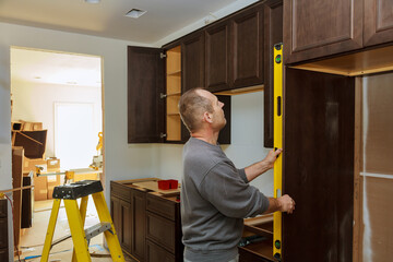 As new kitchen cabinet set is being installed, worker hangs level to ensure that cabinets are level