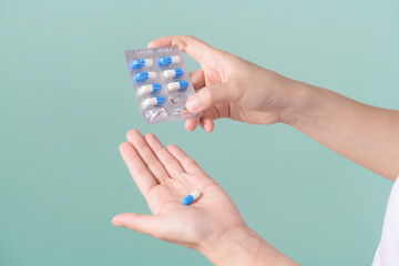 Medical pills. woman hands removing pills from panel on green background.