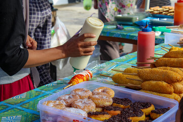 A street vendor puts mayonnaise on corndogs.