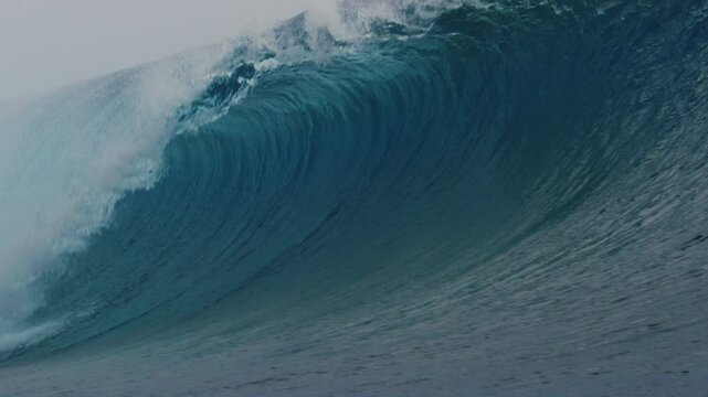 Thick heavy wave from Cloudbreak surf spot crashes in ocean in slow motion as spray rises off top