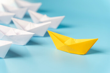 Leadership concept, yellow leader boat leading black boats, on blue background with empty copy space.