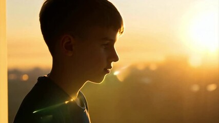 Tracking a young teenage boy's face as he jogs indoors in silhouette against a window with a view out to the sunrise over the city.