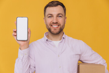 Handsome unshaven man wear shirt casual clothes hold stack cardboard boxes use blank screen mobile cell phone isolated on yellow background studio portrait