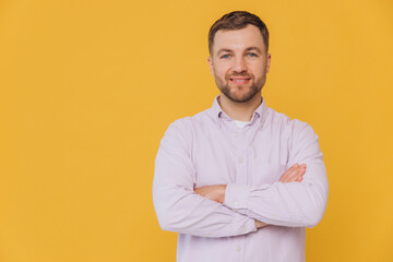 Cute unshaven man smiling with healthy teeth and crossed arms in purple shirt posing isolated on yellow background with copy space