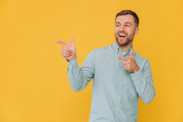 Cute unshaven man in mint shirt pointing fingers up at copy space isolated on yellow background