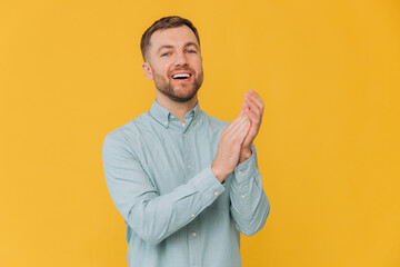 Cute unshaven man in mint shirt clapping hands and applauding isolated on yellow background with copy space