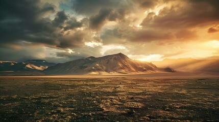 Fototapeta premium A breathtaking view of a rugged mountain range bathed in the warm golden light of a sunset. The vast landscape features barren terrain in the foreground, covered with small patches of grass and rocks.