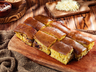 Martabak Manis traditional Indonesian dessert, sliced on a wooden board, with ingredients such as grated cheese and chocolate sauce in the background. The golden brown pastry features a fluffy texture