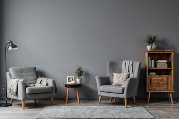 Books and lamp on rustic cupboard next to grey armchair with cushion against a wall with copy space in living room interior