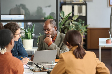 Diverse group of business people sitting at meeting table together and brainstorming ideas with...
