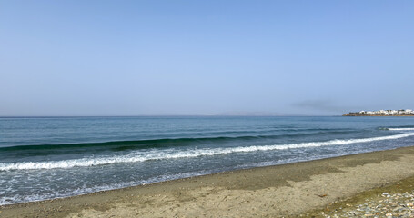 Tinos island, Cyclades Greece. White building, ripple sea, beach with sand, pebble, blue sky.