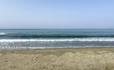 Sandy beach at Greek island. Ripple sea touches wet sand, blue sky background.