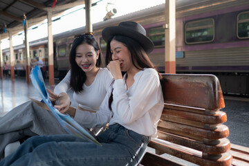 Smiling women on the station platform with happily looking into a smartphone, girls standing at train station take selfie photo on smartphone.