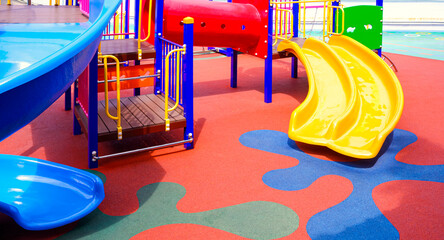 Slides with colorful playground equipment on rubber floor in outdoors playground area at kindergarten