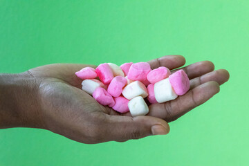 Tasty sweet marshmallows in a woman hand, green background.