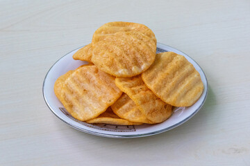 Delicious spicy potato chips on a white plate on wooden background. Alooz crackers sour cream and onion flavor.