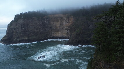 Flying over Rocky Cliffside with Waves Crashing Below and a Foggy Forest Above