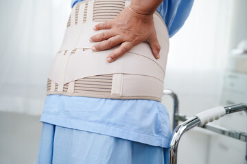 Asian senior pain back wearing elastic support belt with walker.