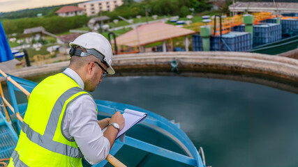 environmental engineer working at the wastewater treatment try to check the quality of the water in a tank and write donw the test result on a clipboard © SAHARAT