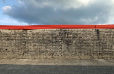 Grunge concrete wall made of small square blocks with red metal strip on top. Dark cloudy sky above, street in front. Background for copy space.