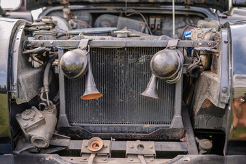 Close-up view of a vintage car's engine compartment, showcasing the radiator and dual horns. Some signs of rust and wear. Some copy space.