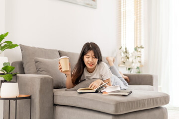 Woman sipping coffee and reading a book on the sofa.