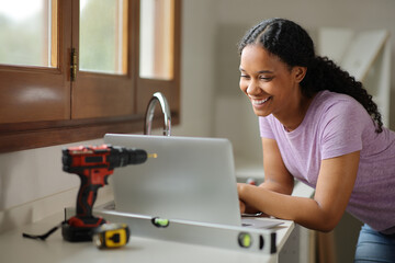 Happy black woman checking laptop reforming house