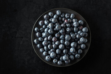 Blueberries in a black plate on a black stone table.