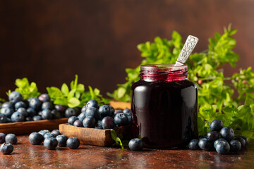 Blueberry jam and fresh berries on a brown background.