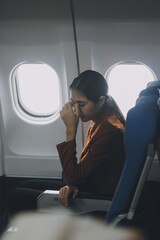 Stressed and serious young asian businesswoman remote working on the plane, suffering from headache and airsick during the flight.