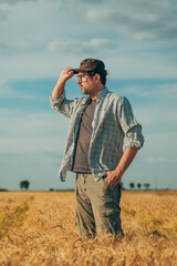 Male farmer standing in ripe wheat field and looking over the harvest ready crops at the horizon and sunny sky