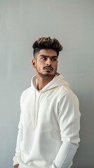 Obraz premium An Indian male model poses in a white hoodie against a grey backdrop