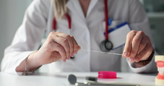 Hygienist woman coils dental floss on fingers at table