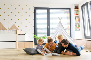 Young nuclear family playing with toys in a living room. Parents and children lying on floor,...