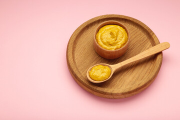 Dijon mustard in bowl and spoon on pink background.