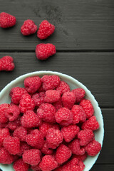 Raspberries on mint plate on black wooden background. Vertical photo